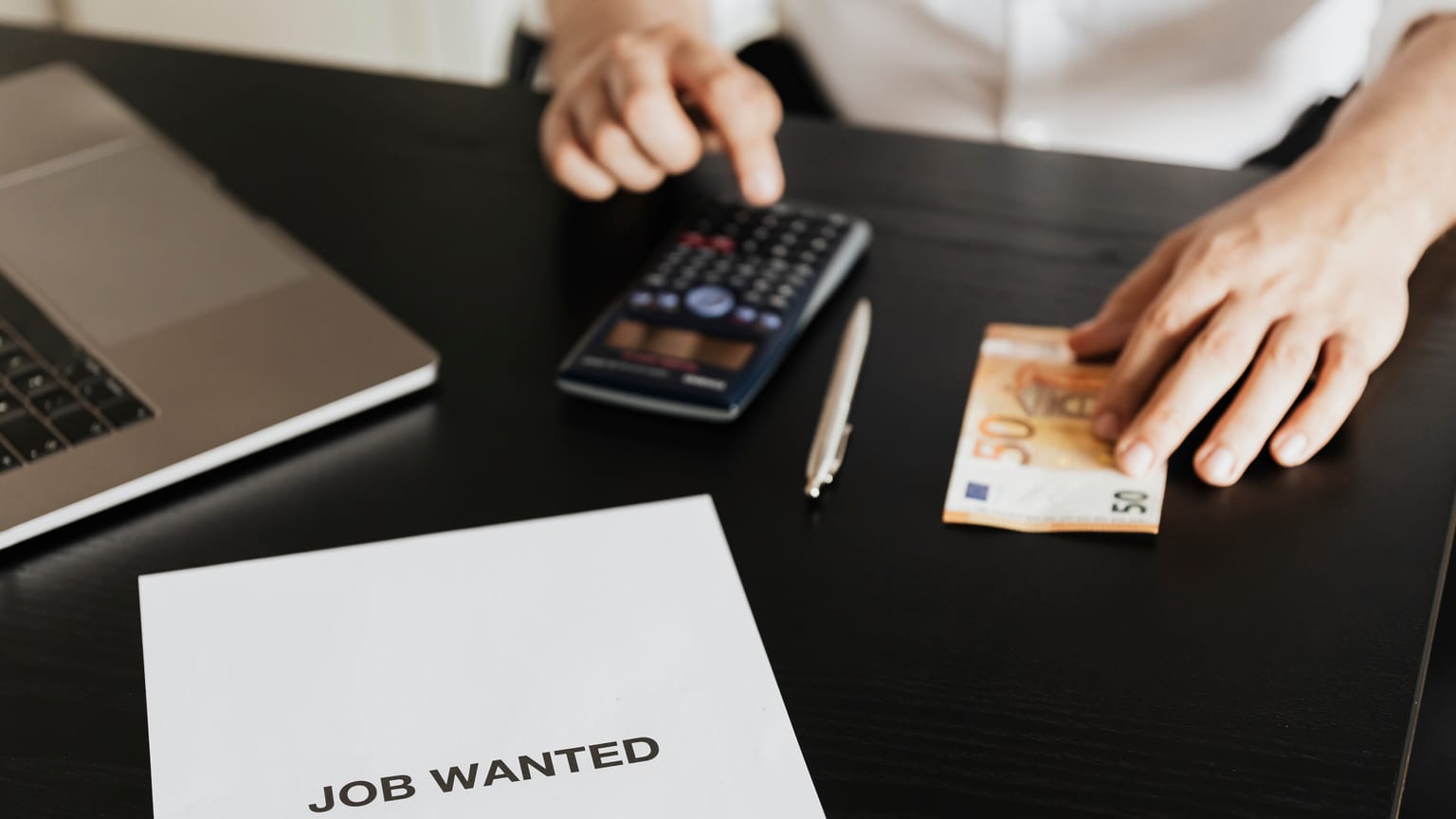 A man using a calculator beside a Job Wanted sheet — entitlement to severance pay after losing a job