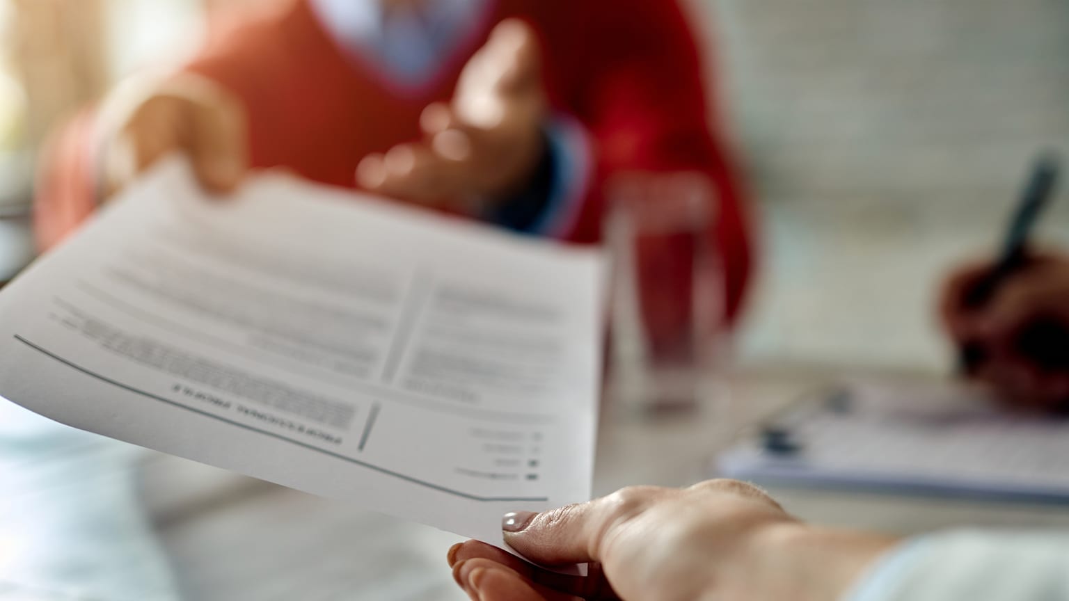 Handing a written document across a desk — a resignation letter and its template